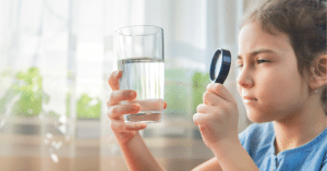Kind untersucht Wasserglas mit einer Lupe